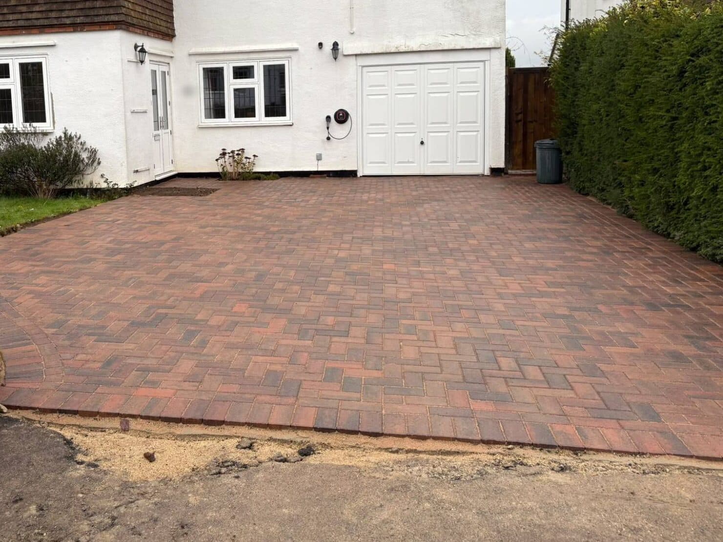Brindle herringbone block paved driveway with a curved border beside a lawn, in front of a white semi-detached house