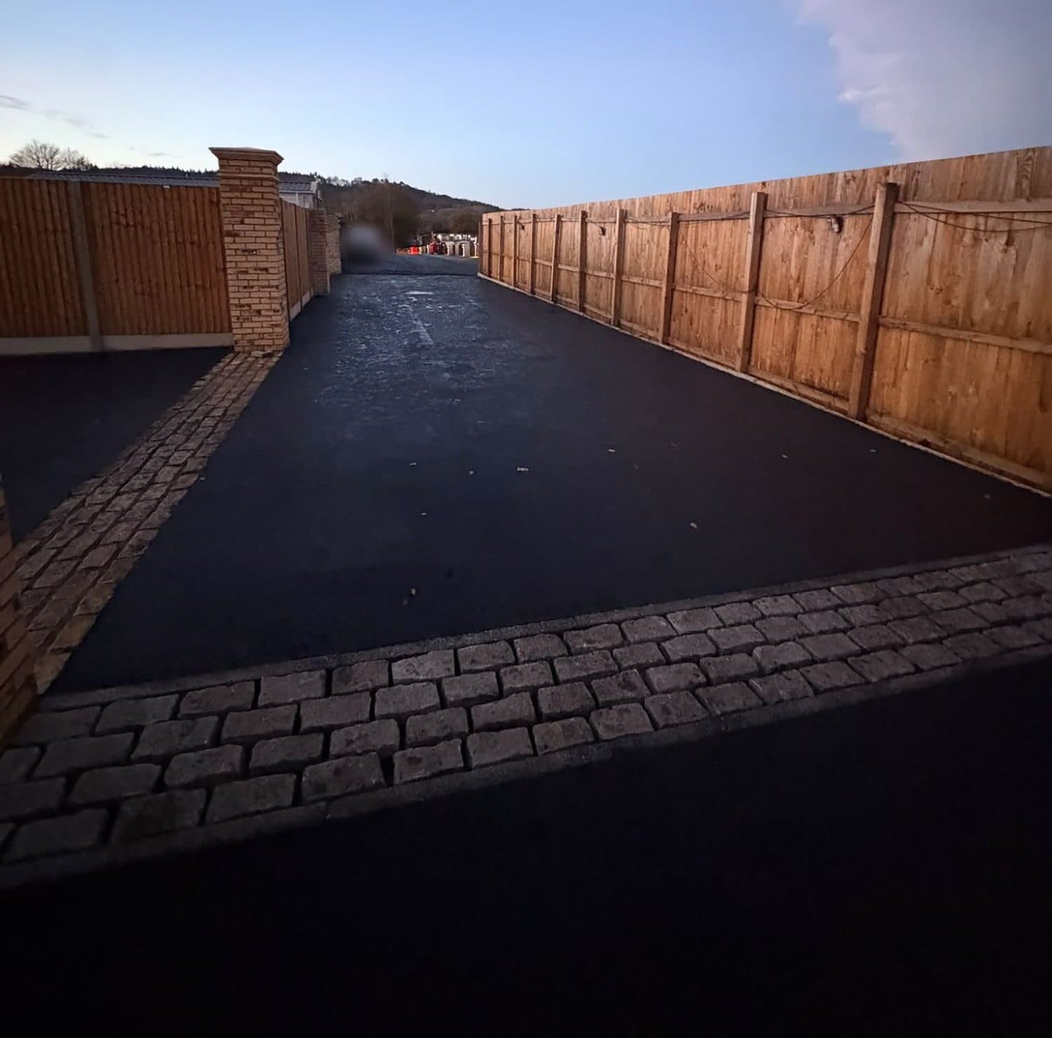 New tarmac driveway between close-board fences, framed by a granite sett border and threshold